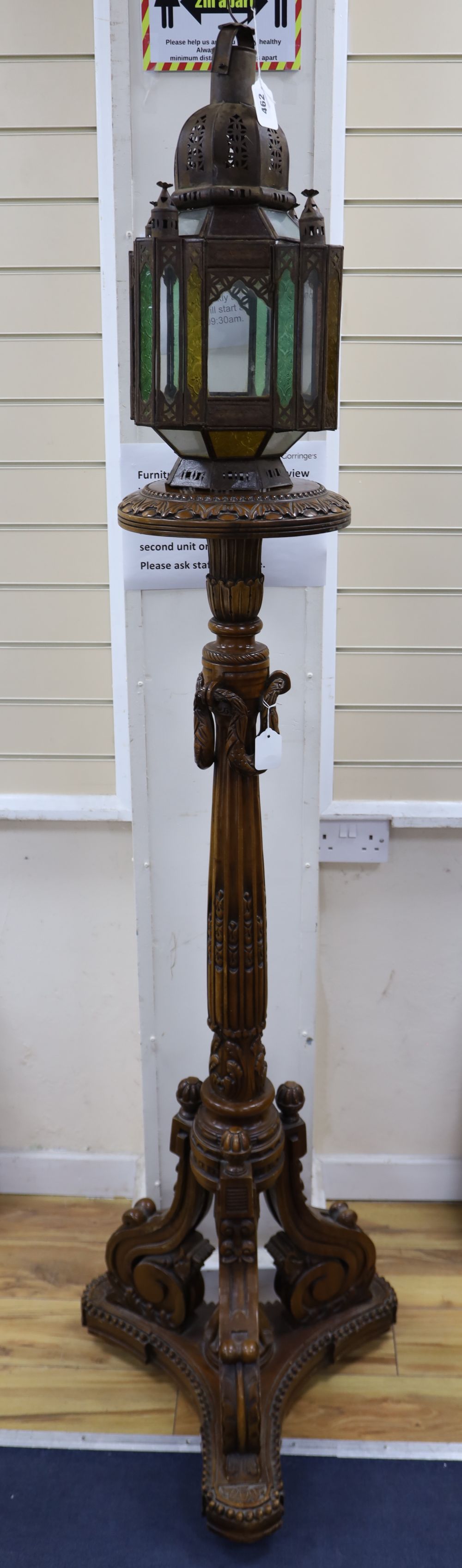 A pierced metal lantern with coloured glass panes, on carved walnut triform pedestal, 206cm overall